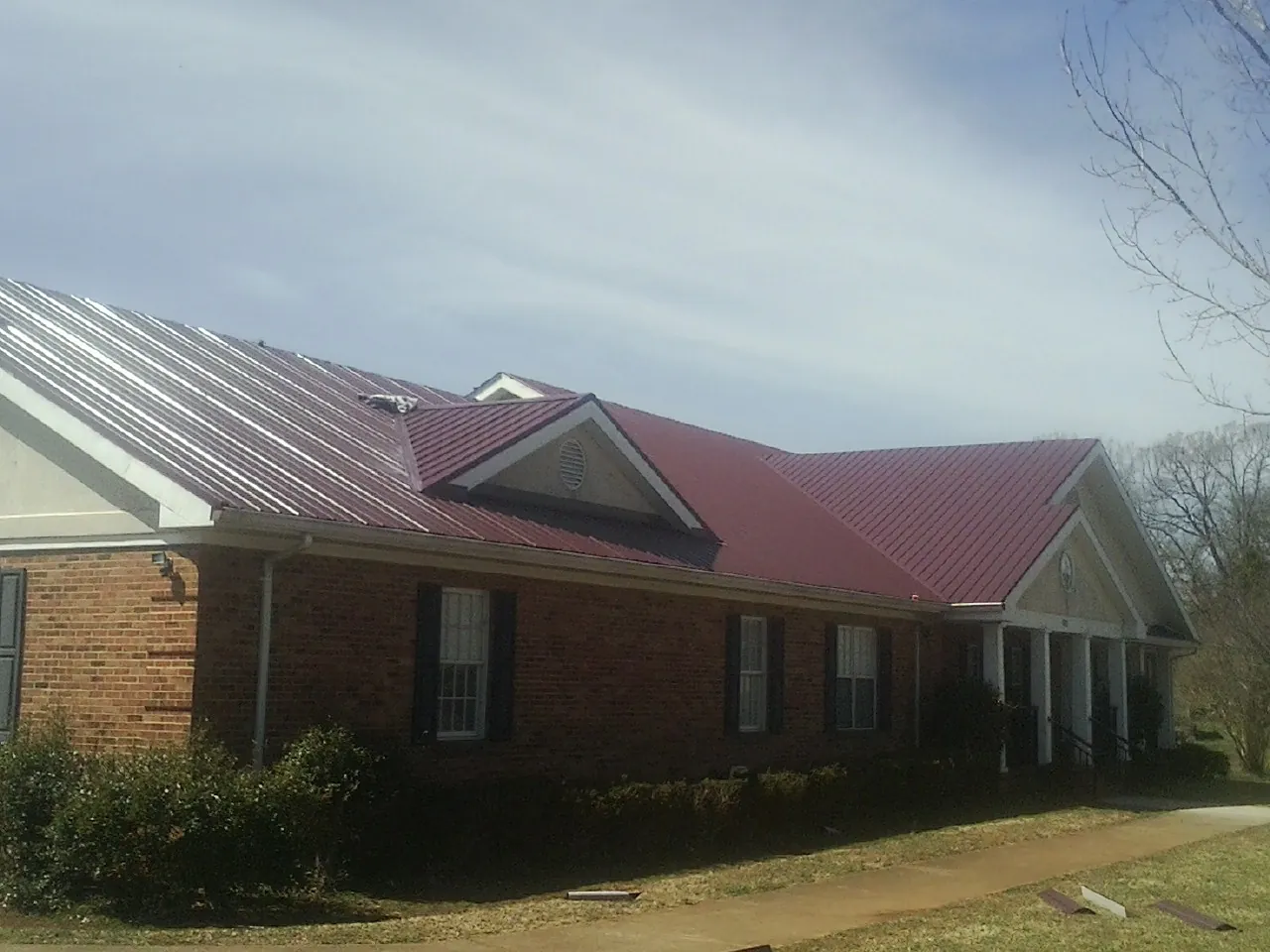 Red metal roof with gabled entries on a long brick building, from a Hail Damage Roof Repair job in Somerset